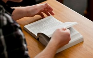 Henkilö tutkii Mormonin Kirjaa pöydällä