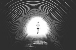 mies kävelee tunnelissa kohti valoa